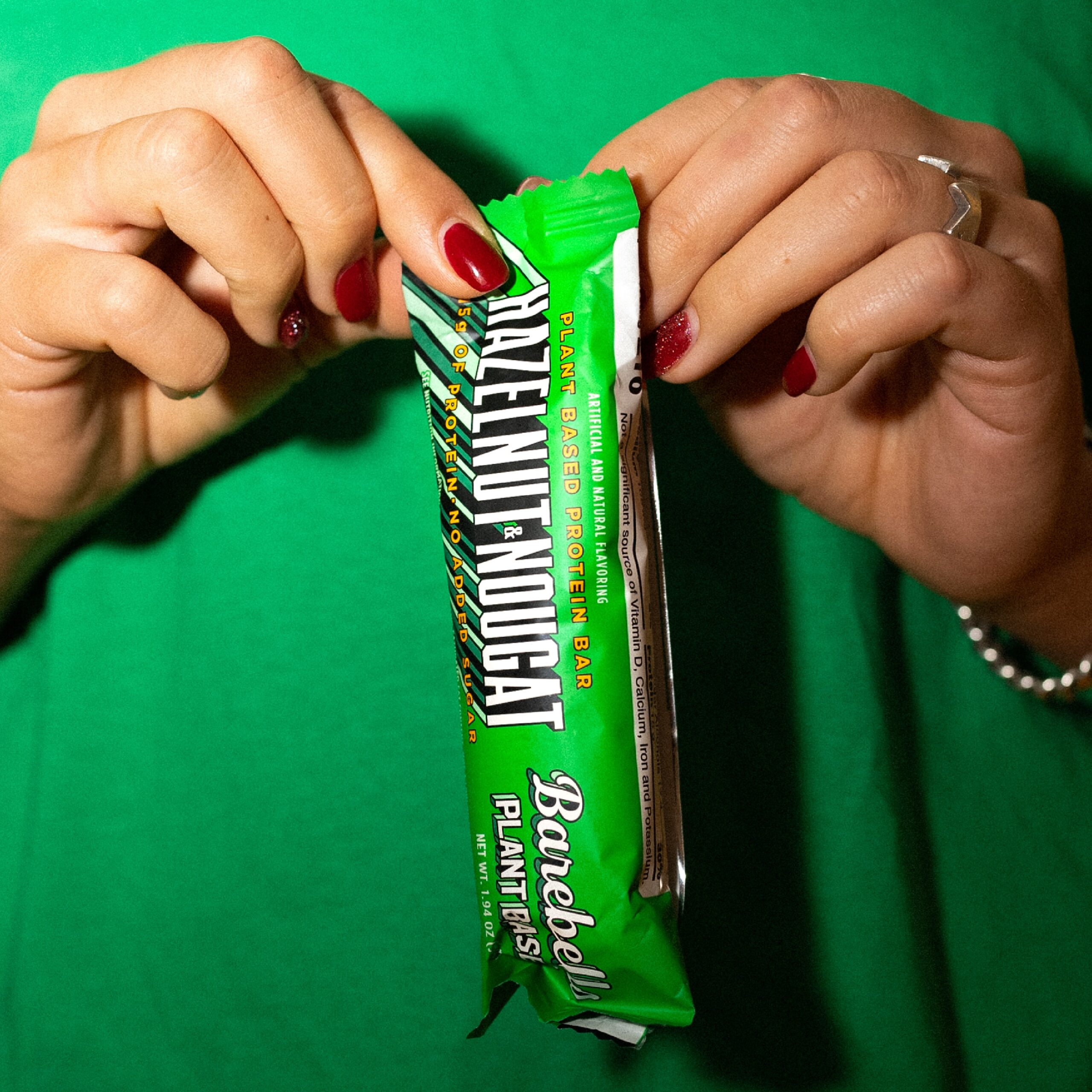 Hands opening a green plant-based protein bar on a green background.